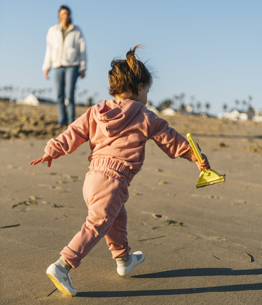  Toddler wearing supportive jbrds first walker shoes and running on a beach.