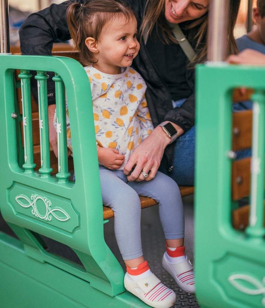  A seated baby wearing jbrds shoes, accompanied by an adult woman.  
