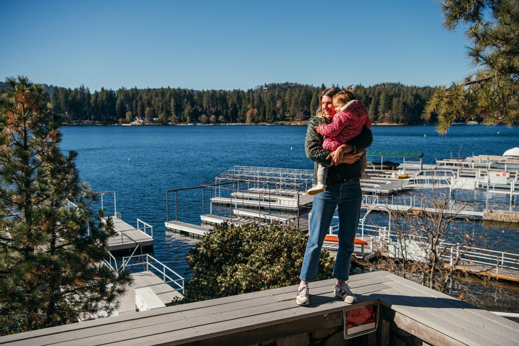 Parent holding their child wearing jbrds shoes while standing on a pier, symbolizing support and growth.