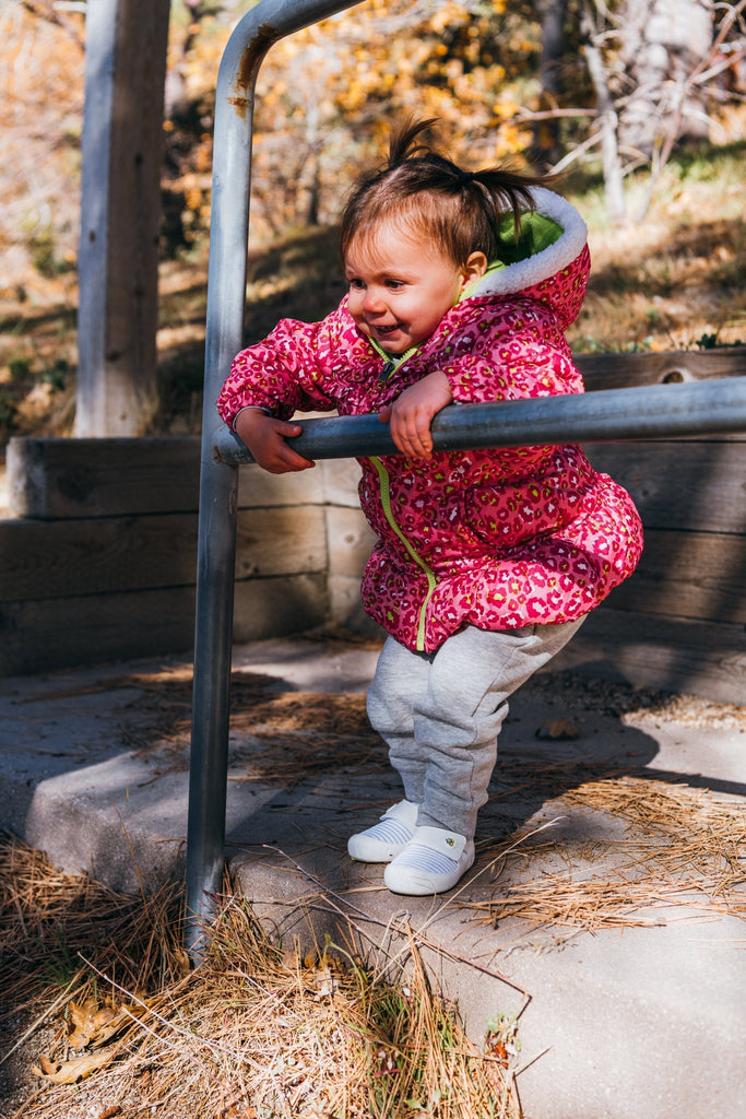 Toddler practicing balance while holding rails, wearing jbrds shoes on a natural outdoor path.