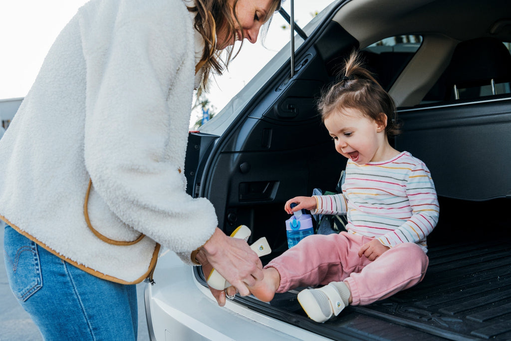 Mother helping her toddler put on properly fitted shoes in a car, focusing on comfort and preventing blisters.