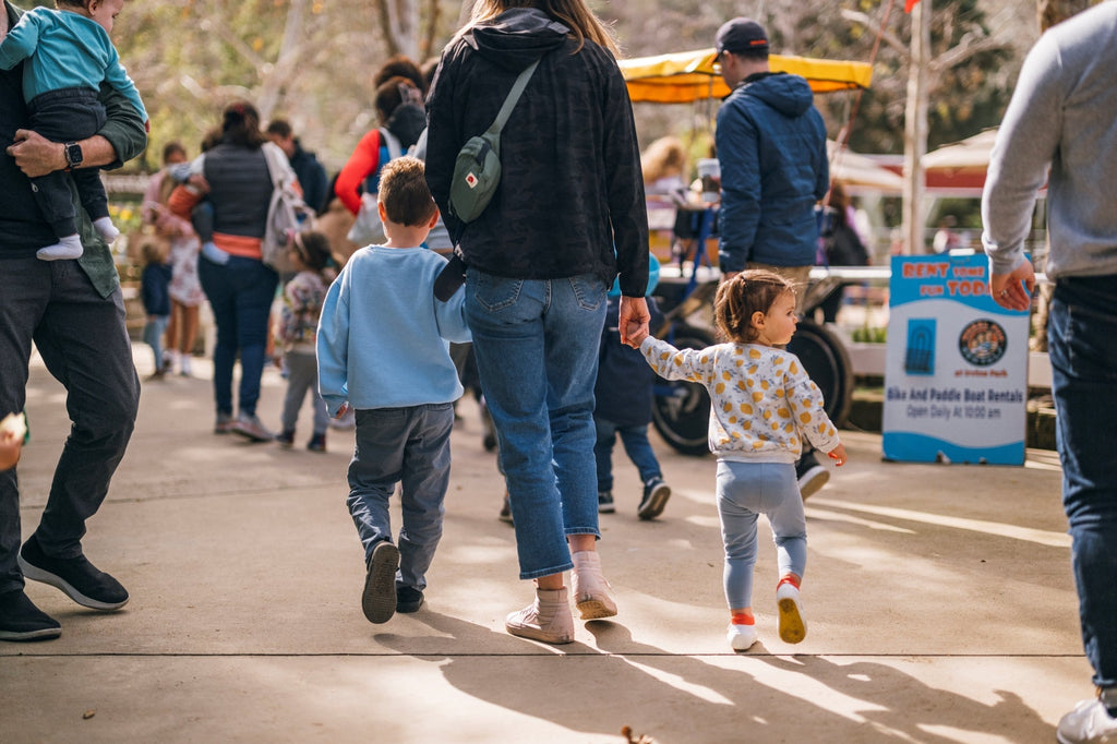 Toddlers exploring outside wearing jbrds Stand2Walk shoes, accompanied by an adult woman. 