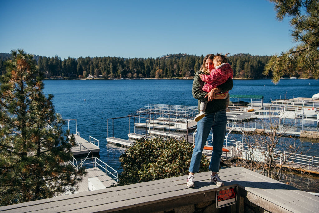 A woman carrying a child in her lap, wearing pediatrician-approved jbrds shoes at a pier.